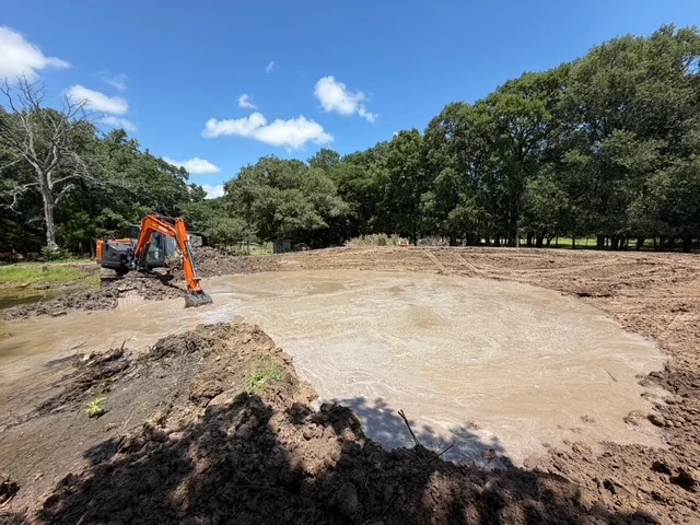 Tracked excavator grading cleared lot with removed soil and debris piles