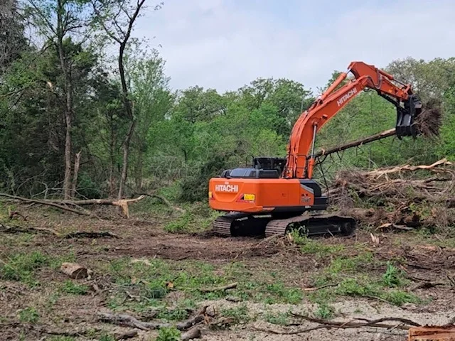 Orange Hitachi excavator with mulching head clearing wooded land and processing tree debris