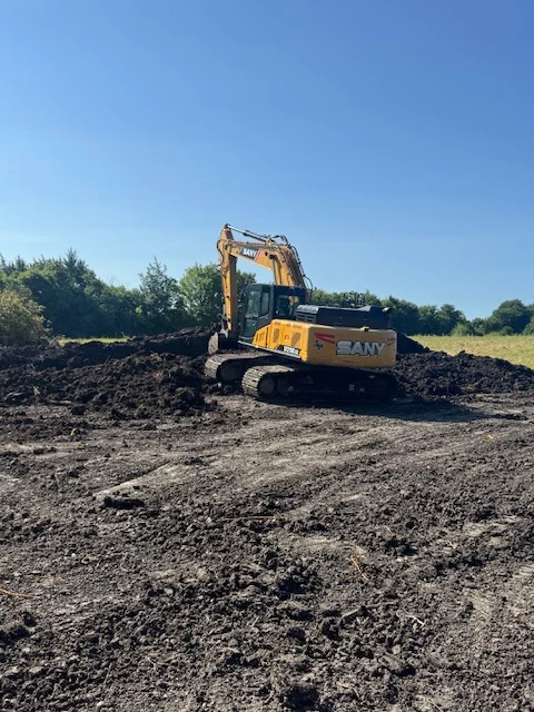 Yellow tracked excavator working on compacted soil and aggregate material at open site