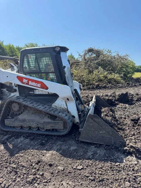 Bobcat track loader with bucket on excavated site with graded earth and stone material