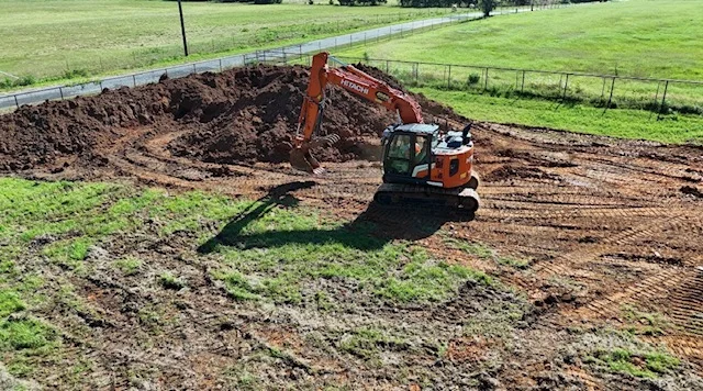 Tracked excavator with bucket attachment moving soil and creating material stockpiles on cleared land