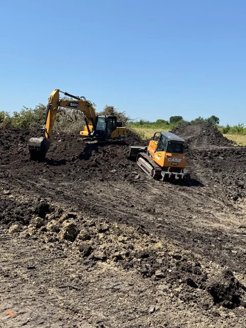 Tracked excavator and compact loader moving earth materials on cleared excavation site