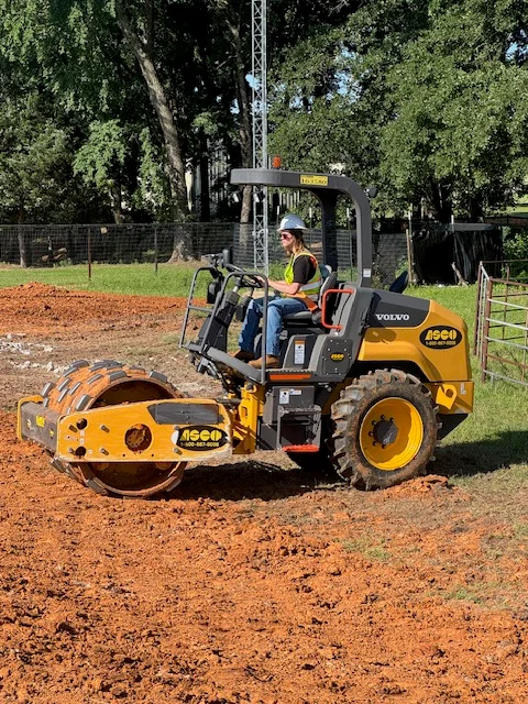 Volvo vibratory roller compacting reddish-brown soil on residential driveway