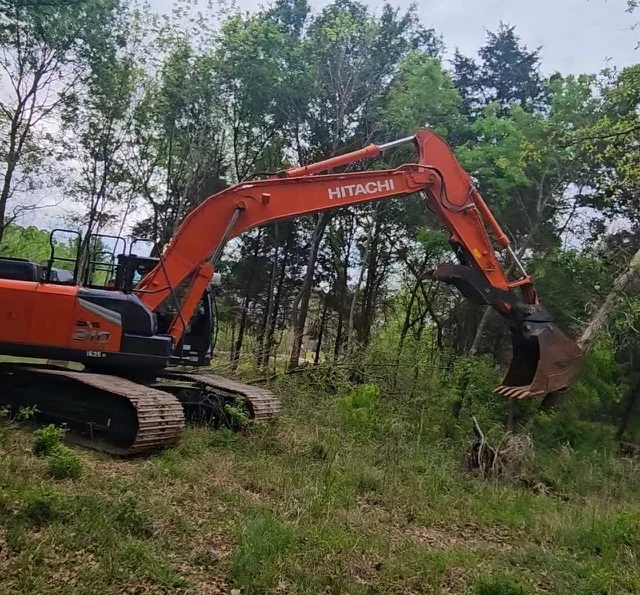 Red Hitachi tracked excavator clearing vegetation and brush from wooded site