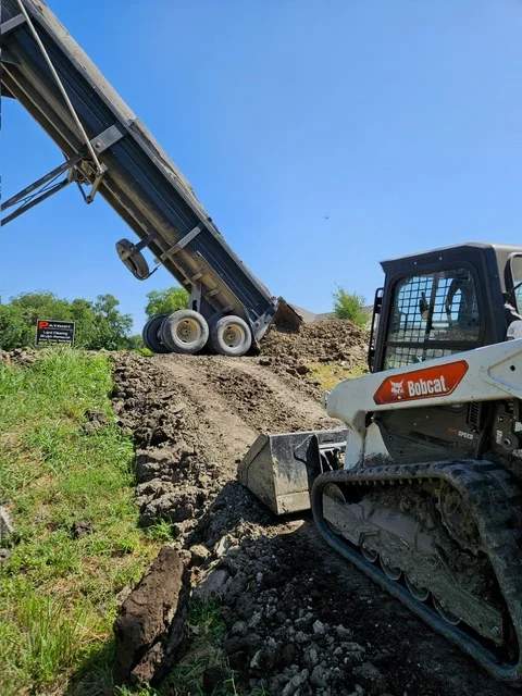Dump truck unloading aggregate, Bobcat skid steer loader spreading material on site