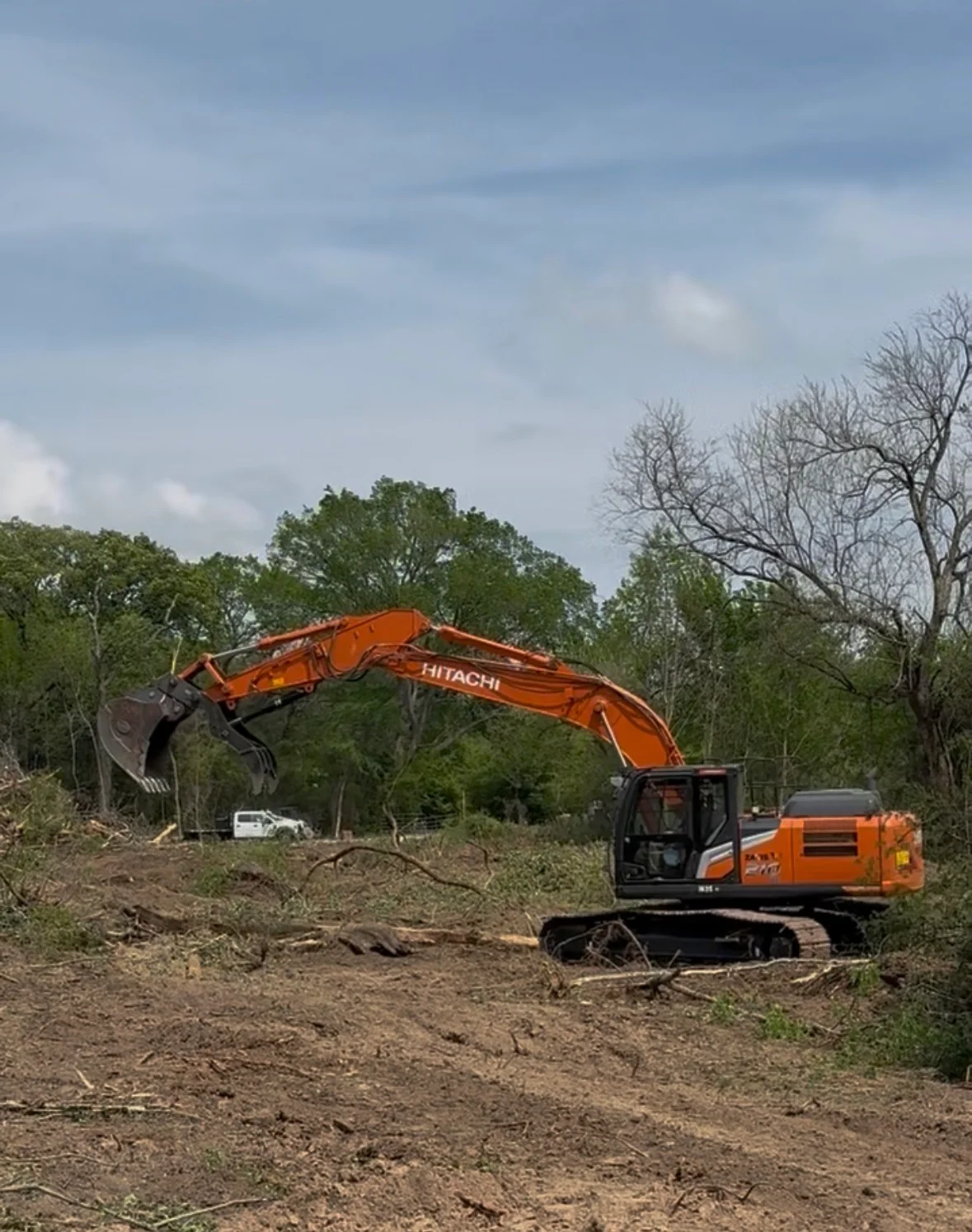 Hitachi excavator with bucket clearing vegetation and brush from wooded site