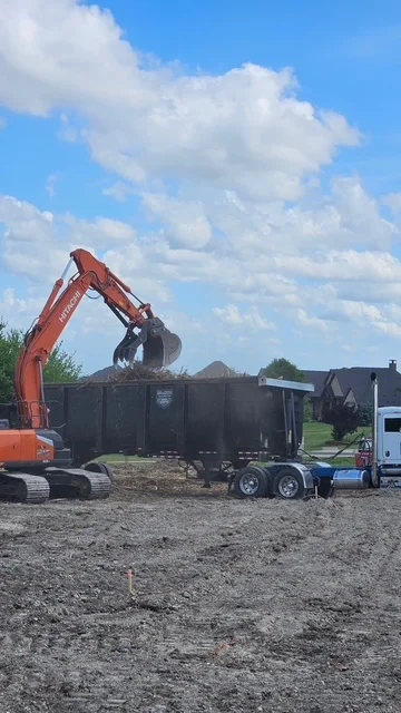 Excavator loading aggregate into open-bed trailer on job site