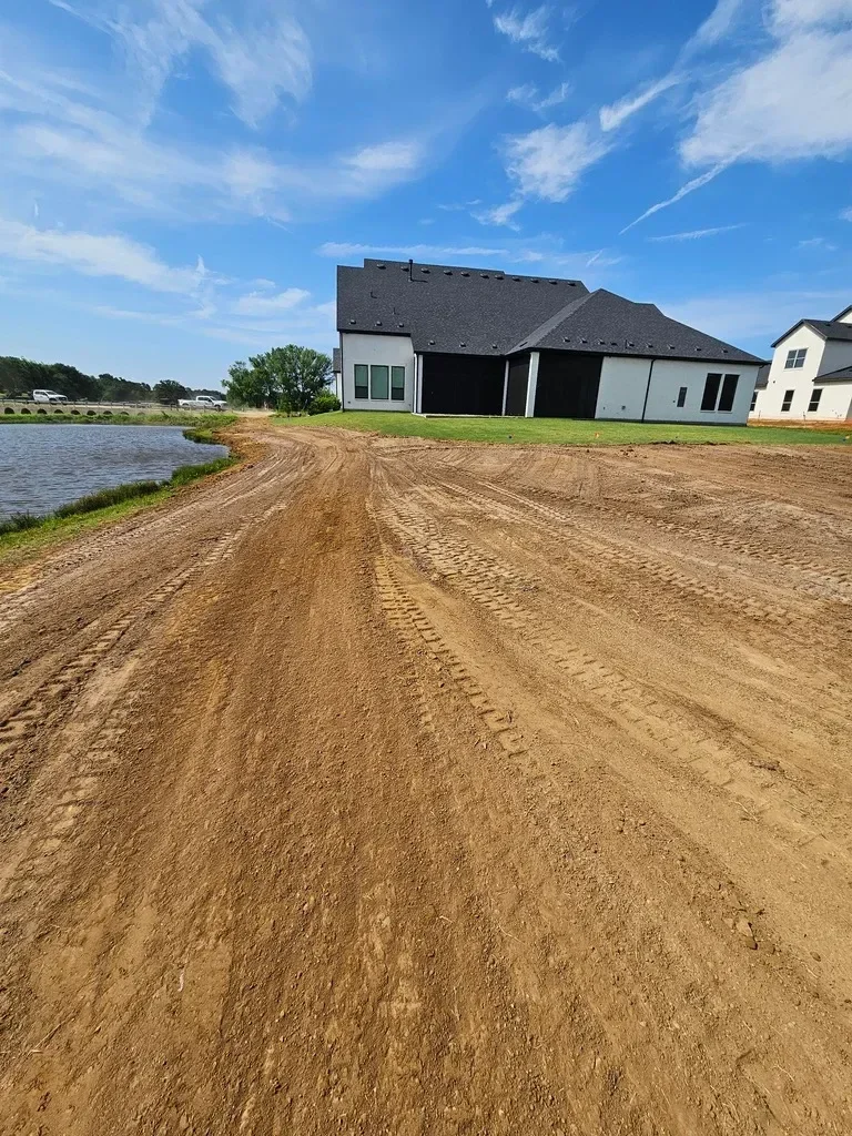 A freshly final-graded residential lot in Dallas, Texas showing a smooth, evenly sloped soil surface ready for sod installation. The graded area slopes away from the home's foundation with no visible pooling or erosion channels.