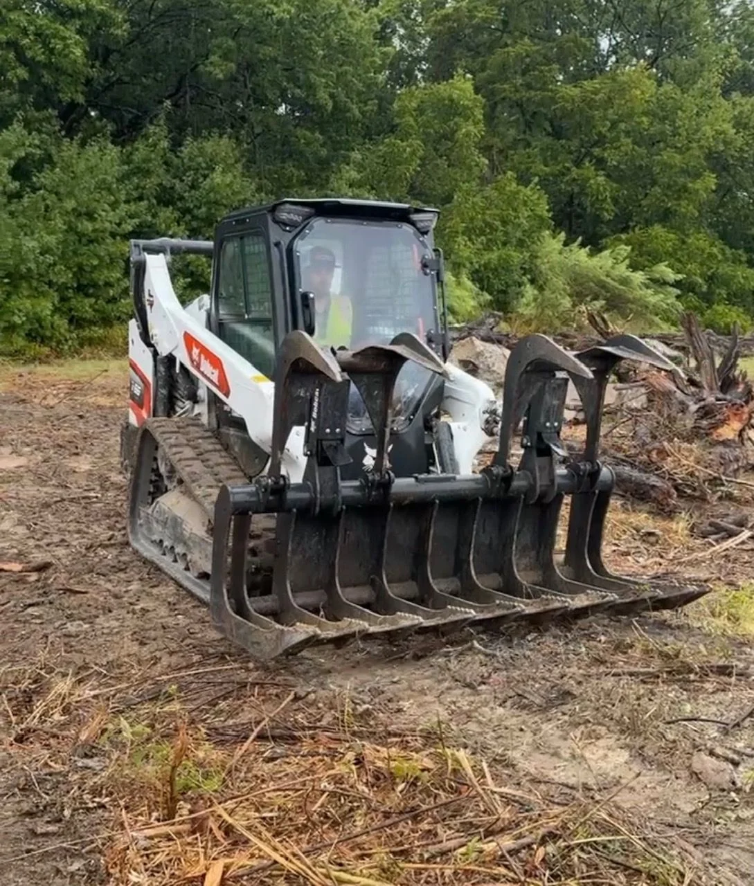 A heavy equipment push crew clearing a large pile of storm debris and downed tree limbs from a commercial lot in Dallas, Texas. The operator uses a bulldozer to consolidate scattered material into a staged pile near the property edge.